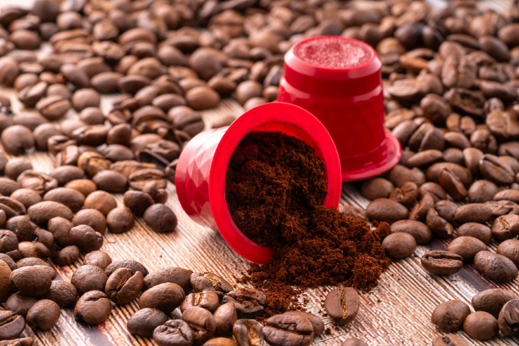 Two red coffee pods, one open and overturned, sit among a lot of coffee beans - keurig k-cups