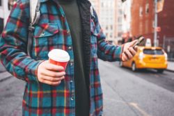 person with coffee and cell regarding the Tim Hortons mobile tracking class action lawsuit 