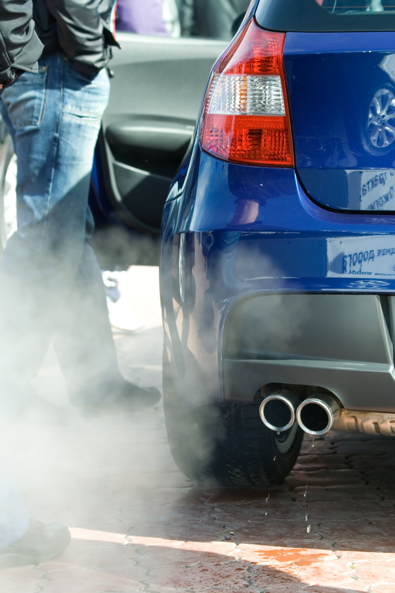Person standing next to car emitting exhaust regarding the Bosch emissions cheating device class action settlement 