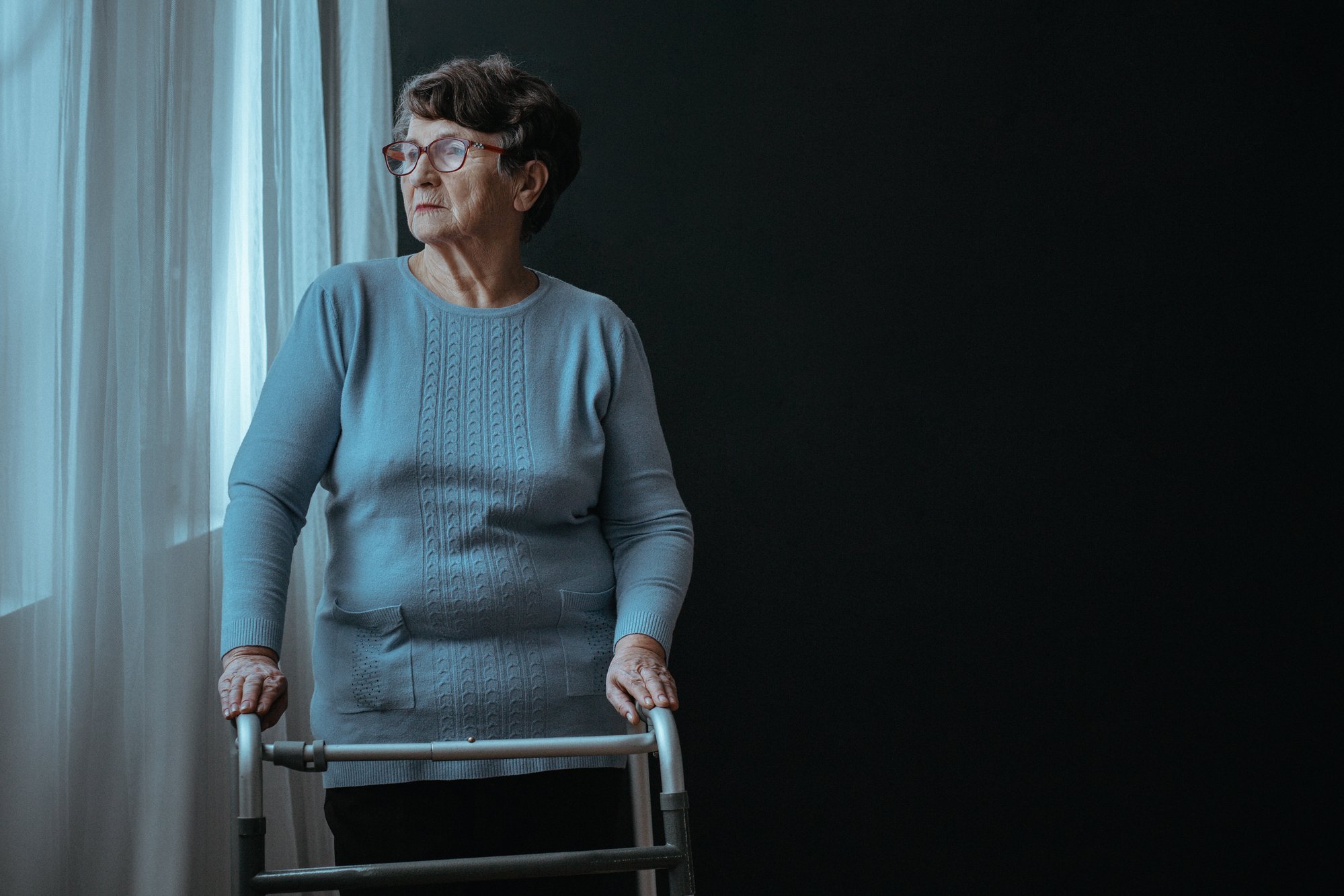Woman standing in window with walker regarding the nursing home class action lawsuit filed after 31 senior deaths 