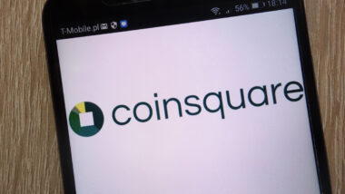 Coinsquare logo displayed on a modern smartphone against a wooden background.