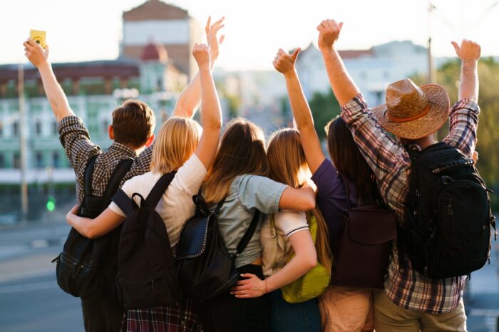 Student travelers with backpacks rising hands, joy and positivity