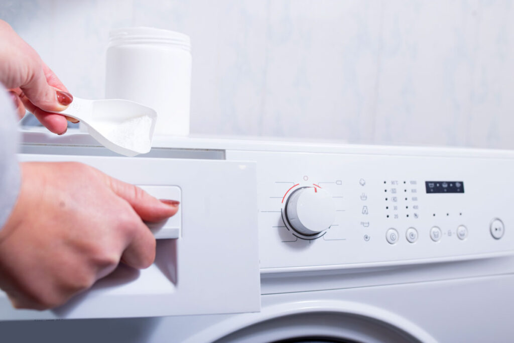 Close up of a woman's hand putting laundry detergent in a washing machine.