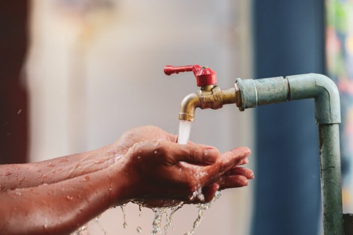 The hand is supporting the water from the tap. Choose focus on the faucet