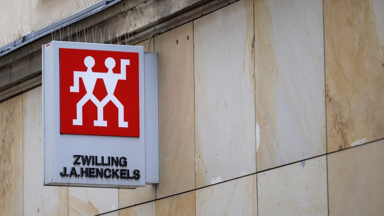 Zwilling J.A. Henckels storefront sign with the red twin figures logo is mounted on a stone building facade in an urban setting.