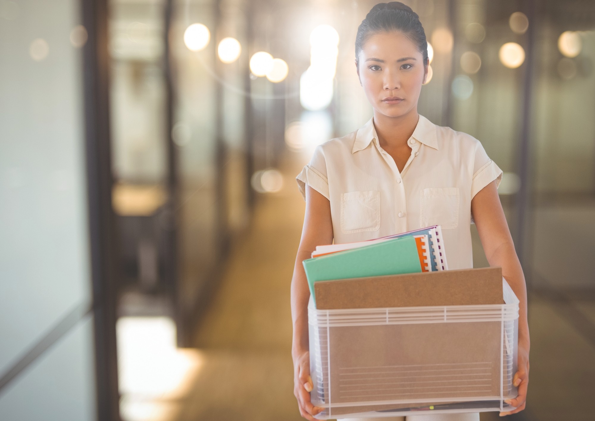 Woman looking unhappy holding a box with her things regarding the temporary layoffs underway amid COVID-19 pandemic 