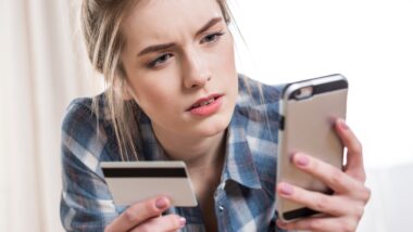 A woman looks concerned while trying to make a payment using a credit card on her smartphone - amex prepaid